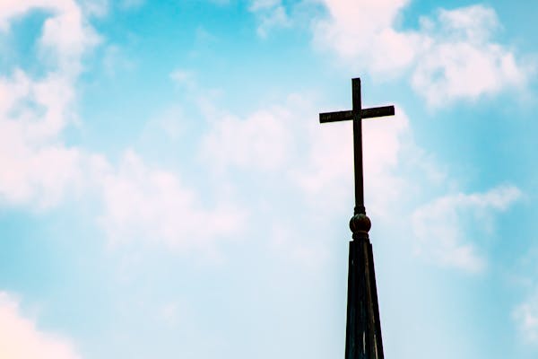 A church spire with a cross silhouetted against a bright blue sky with clouds.